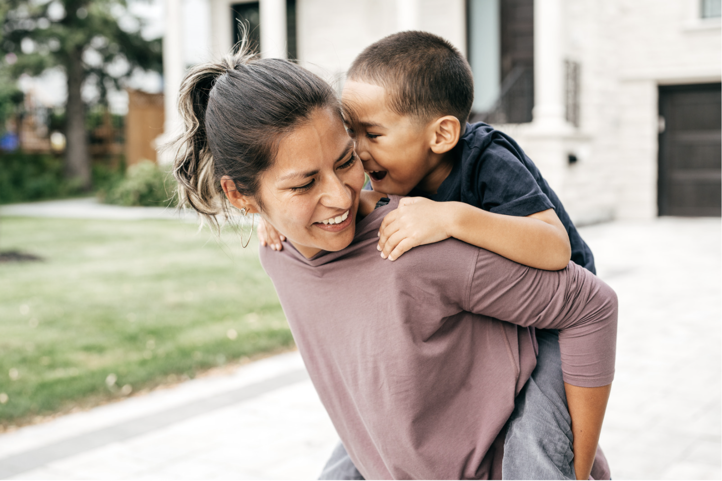 Happy mom giving her excited 4-year-old son a piggyback ride in the driveway; both smiling and enjoying a playful, mindful parenting moment outdoors.