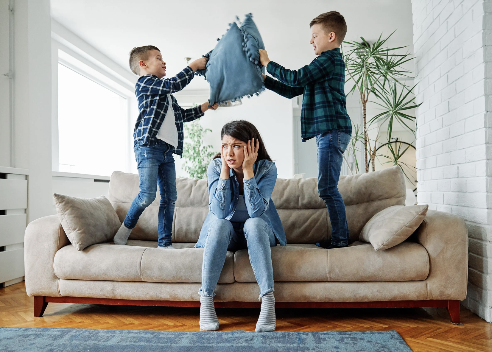 Stressed mom sitting on a couch as two boys have a pillow fight, works to find calm as a mom.